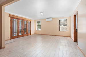 Empty room featuring french doors, crown molding, light wood-style floors, and a wall mounted AC