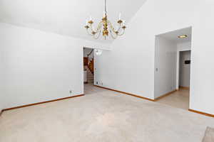 Empty room with high vaulted ceiling, a chandelier, light colored carpet, and stairway