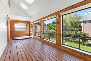 Unfurnished sunroom featuring a skylight, wood walls, hardwood / wood-style flooring, and high vaulted ceiling