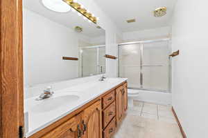 Full bathroom with shower / bath combination with glass door, double vanity, and light tile patterned floors