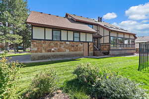 Rear view of property with roof with shingles, a lawn, and stone siding