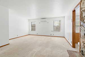 Unfurnished room with plenty of natural light, light carpet, a textured ceiling, and a wall mounted AC