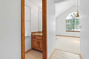 Corridor featuring vaulted ceiling, a chandelier, light carpet, and light wood-style flooring