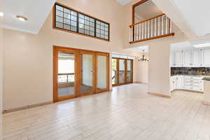 Unfurnished living room with a chandelier, a high ceiling, plenty of natural light, light wood-style flooring, and french doors