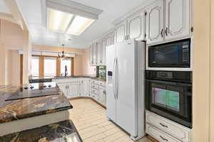 Kitchen with black appliances, dark stone countertops, a chandelier, pendant lighting, and white cabinetry