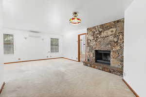 Unfurnished living room featuring a stone fireplace, carpet flooring, and a wall mounted AC