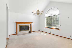 Unfurnished living room featuring a tiled fireplace, a chandelier, carpet floors, and high vaulted ceiling