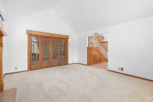 Unfurnished living room with high vaulted ceiling, light carpet, and stairway