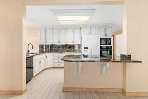 Kitchen with a peninsula, dark stone counters, a kitchen breakfast bar, black appliances, and light wood-style floors