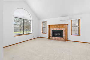 Unfurnished living room with carpet flooring, a wall unit AC, a tile fireplace, and high vaulted ceiling