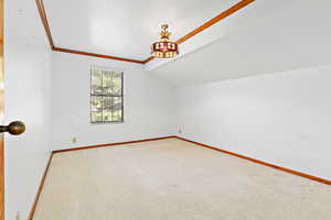 Spare room featuring ornamental molding, carpet floors, and vaulted ceiling
