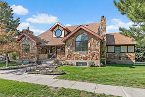 Tudor house featuring stone siding, a shingled roof, a front yard, and a chimney