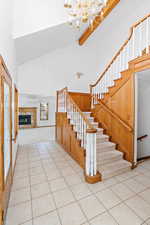 Foyer entrance with high vaulted ceiling, a glass covered fireplace, a chandelier, light tile patterned flooring, and beam ceiling