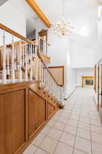 Entrance foyer with stairway, beam ceiling, light tile patterned floors, a chandelier, and high vaulted ceiling