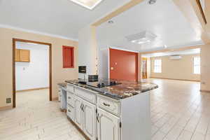 Kitchen with open floor plan, light wood-style flooring, dark stone counters, crown molding, and black electric cooktop