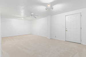 Unfurnished room featuring a textured ceiling, light carpet, and ceiling fan