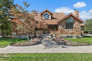 View of front of property featuring stone siding, a chimney, a front yard, and roof with shingles