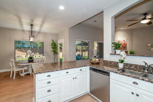 Kitchen with a peninsula, dishwasher, dark stone countertops, decorative light fixtures, and white cabinetry