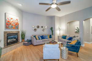 Living area featuring wood finished floors, a fireplace, a ceiling fan, and arched walkways