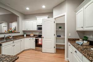 Kitchen featuring stainless steel appliances, white cabinets, dark stone countertops, light wood-style floors, and recessed lighting