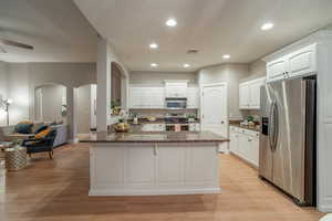 Kitchen featuring stainless steel appliances, recessed lighting, white cabinetry, light wood finished floors, and arched walkways