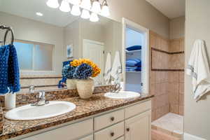 Full bath featuring tiled shower and double vanity