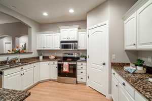 Kitchen featuring appliances with stainless steel finishes, white cabinetry, dark stone counters, light wood-style flooring, and recessed lighting