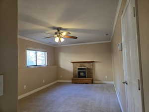 Unfurnished living room with crown molding, carpet, a brick fireplace, and a ceiling fan