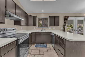 Kitchen featuring appliances with stainless steel finishes, dark brown cabinets, a peninsula, under cabinet range hood, and french doors