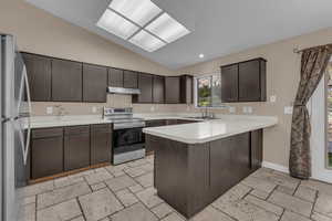 Kitchen featuring a peninsula, dark brown cabinets, stainless steel appliances, vaulted ceiling, and light countertops