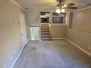 Unfurnished living room with crown molding, carpet floors, a ceiling fan, and stairway