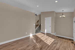 Unfurnished living room with wood finished floors, stairway, recessed lighting, and a chandelier