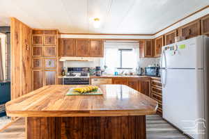 Kitchen with white appliances, brown cabinetry, a textured ceiling, wooden counters, and under cabinet range hood