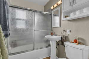 Bathroom with combined bath / shower with glass door and a textured wall