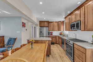 Kitchen featuring appliances with stainless steel finishes, brown cabinets, light wood-type flooring, tasteful backsplash, and recessed lighting