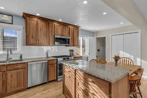 Kitchen with light wood-style floors, light stone counters, appliances with stainless steel finishes, backsplash, and recessed lighting