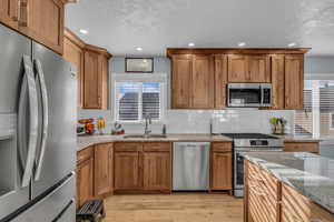 Kitchen with appliances with stainless steel finishes, light wood-style flooring, tasteful backsplash, light stone counters, and a textured ceiling