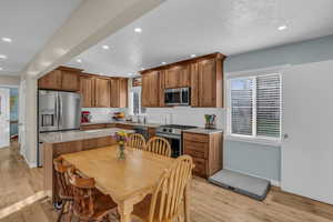 Kitchen with brown cabinetry, appliances with stainless steel finishes, light wood-style floors, light stone countertops, and recessed lighting