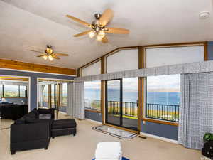 Carpeted living room featuring a water view, vaulted ceiling, plenty of natural light, a textured ceiling, and ceiling fan