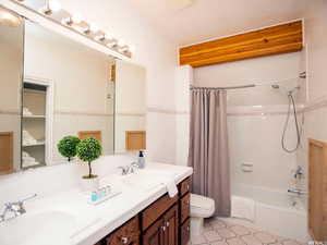 Full bath with shower / bathtub combination with curtain, double vanity, tile walls, light tile patterned floors, and decorative backsplash