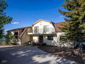 View of front of property with a gambrel roof, roof with shingles, and a balcony
