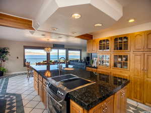 Kitchen featuring stainless steel range with electric stovetop, decorative light fixtures, light tile patterned floors, an island with sink, and dark stone counters