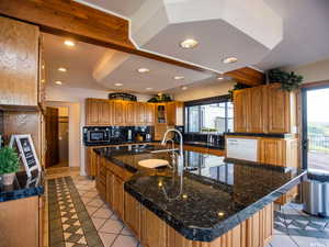 Kitchen featuring brown cabinets, glass insert cabinets, recessed lighting, a kitchen island with sink, and light tile patterned flooring