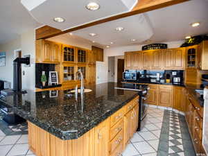 Kitchen with glass insert cabinets, decorative backsplash, brown cabinetry, an island with sink, and recessed lighting