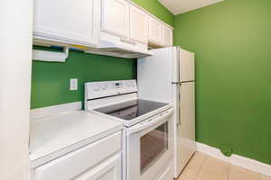 Kitchen with white appliances, white cabinets, light tile patterned floors, under cabinet range hood, and light countertops
