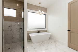 Bathroom featuring plenty of natural light, a marble finish shower, a freestanding bath, light marble finish floors, and tile walls