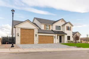 Modern farmhouse with decorative driveway, stone siding, and a garage
