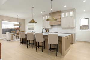 Kitchen featuring glass insert cabinets, pendant lighting, a breakfast bar area, backsplash, and a kitchen island with sink