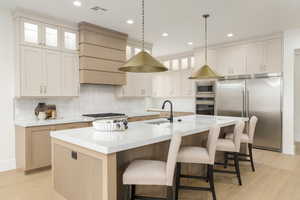 Kitchen featuring glass insert cabinets, tasteful backsplash, built in appliances, light wood finished floors, and a kitchen breakfast bar