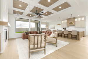 Living area featuring coffered ceiling, beam ceiling, a fireplace, light wood-style floors, and ceiling fan